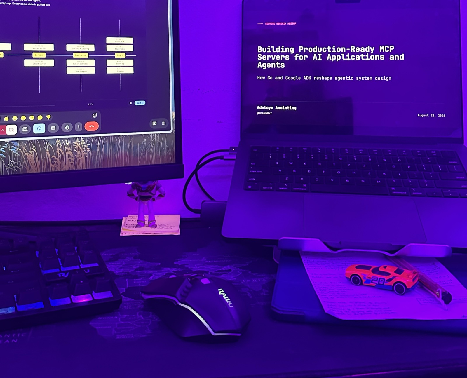 A desk lit purple: a monitor showing the meeting with someone else's slide up, and a laptop with my title slide — Building Production-Ready MCP Servers for AI Applications and Agents.